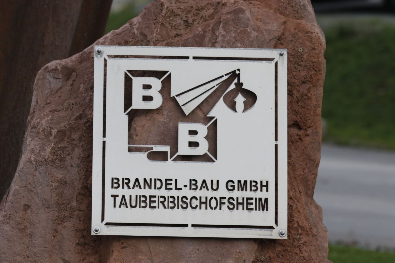 Metallschild mit Stanz des Logos. Befestigt auf einem Stein